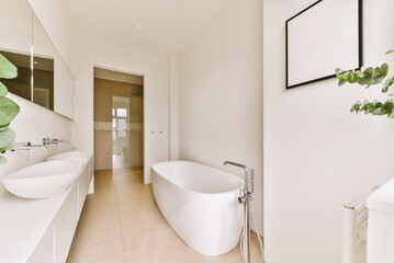 a white bathroom with two sinks and a large plant in the corner on the right side of the bathtub