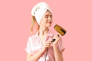 Young woman in towel with hair dryer on pink background