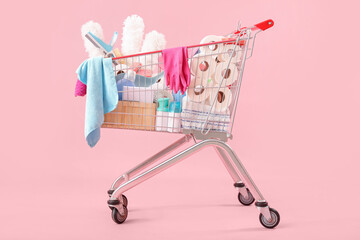 Shopping cart full of cleaning supplies on pink background