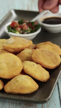 Sopaipillas hand place pebre, pumpkin or squash in rectangular plate on wooden table, bowl of chancaca. Vertical video. Concept of typical Chilean food