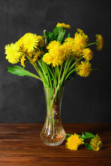 Vase with beautiful dandelion flowers on wooden table against dark background