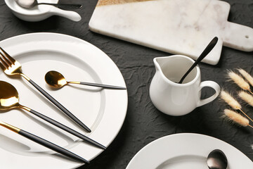 Table setting with clean plates, cutlery and pitcher on black background