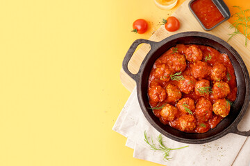 Frying pan of tasty meat balls with tomato sauce and dill on yellow background