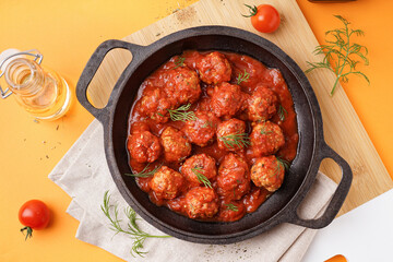 Frying pan of tasty meat balls with tomato sauce and dill on yellow background