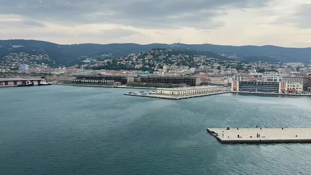 The city skyline of Trieste in Italy. Wind makes waves in the sea and there is a lot of traffic in the city. Time lapse