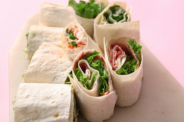 Board of tasty lavash rolls with sausages and greens on pink background