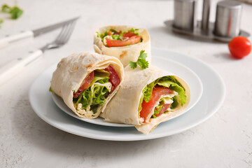 Plates of tasty lavash rolls with tomatoes and greens on light background