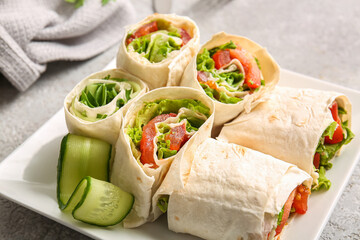 Plate of tasty lavash rolls with vegetables on grey background
