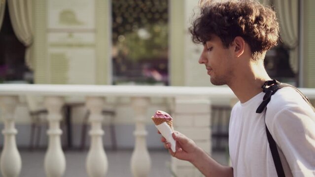 Arabic man eating ice cream in cone while walking on Rome streets. Concept of happy summer vacations, traveling famous landmarks