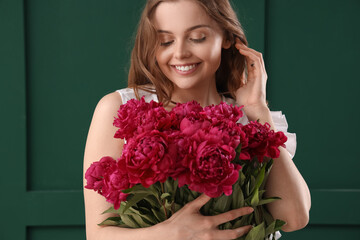 Beautiful young woman with bouquet of peony flowers on green background