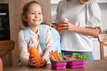 Mother packing school lunch for her little daughter in kitchen