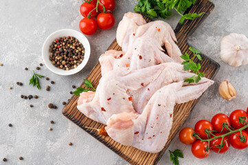 Raw chicken wings on a wooden cutting board with spices, fresh herbs, tomatoes on a gray concrete background. Close up.