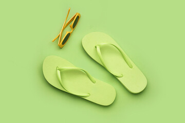 Green flip-flops with sunglasses on color background