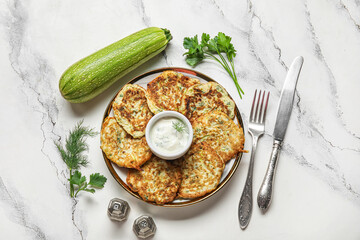 Plate of tasty zucchini fritters with sour cream on white marble background