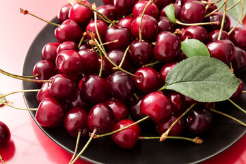Plate with sweet cherries on red background