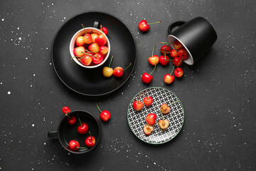 Cups and plates with sweet cherries on black background
