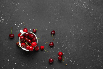 Cup with sweet cherries on black background