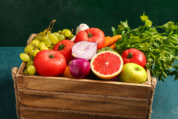 Wooden box with different fresh fruits and vegetables on green background