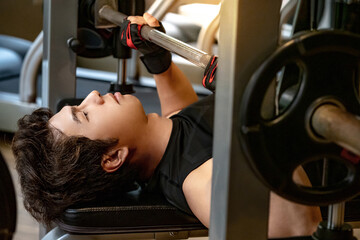Active Asian sport man in black sportswear lying on exercise bench doing barbell bench press...