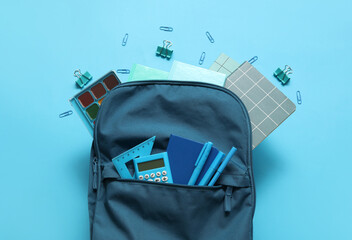 Naklejka premium School backpack with notebooks, calculator and watercolors on blue background
