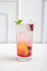 Glass of tasty cherry lemonade with lime and mint on white background