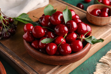 Bowls and board with sweet cherries on green background