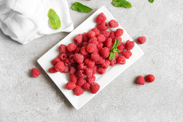 Plate with fresh raspberries and mint on grey background