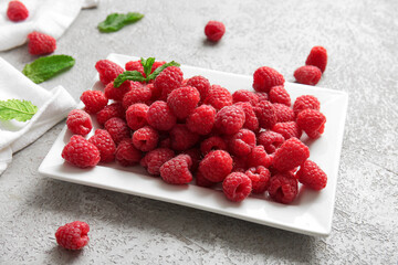 Plate with fresh raspberries and mint on grey background