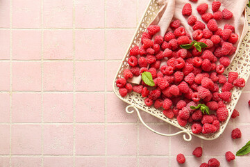 Tray with fresh raspberries and mint on pink tile background