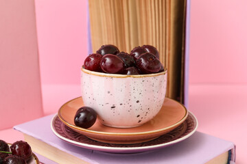 Cup with sweet cherries and books on pink background