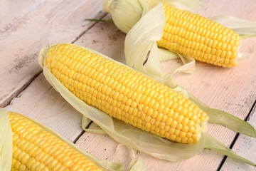 Fresh corn cobs on white wooden background