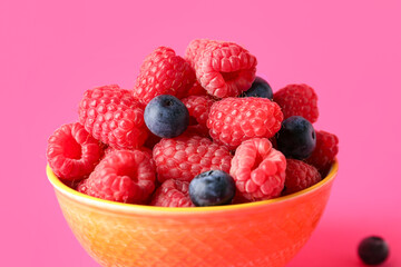 Bowl with fresh raspberries and blueberries on pink background