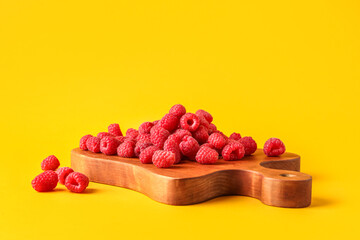 Wooden board with fresh raspberries on yellow background
