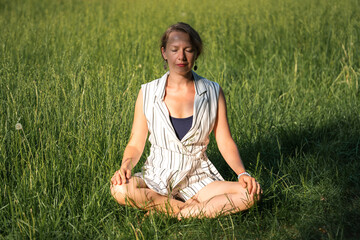 A young blonde woman meditates on the grass in the park during a lunch break.