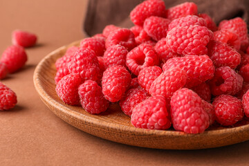 Plate with fresh raspberries on brown background