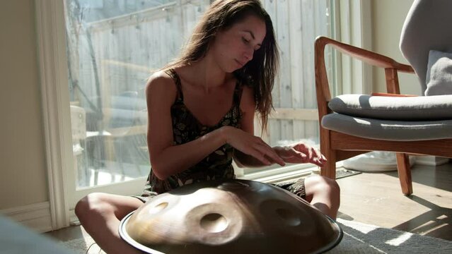 Woman playing steel handpan instrument on sunny morning in living room