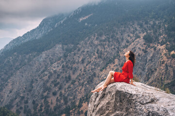 Romantic photo of a girl in a red dress on top of a cliff admiring the view of a mountain gorge