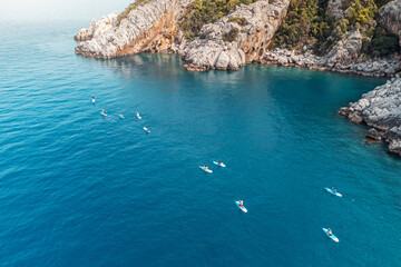 Aerial view of a group or team with paddles swims on a SUP boards on the sea near scenic rocks....