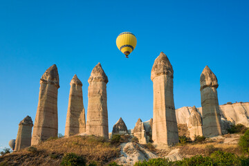 Love Valley in Cappadocia, Yellow hot air balloon flies over unique geological formations, famous...