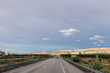 Beautiful summer landscape with highway among rocky mountains and dark blue sky with fluffy clouds on a summer day at sunset. American Roadscape with red canyons in New Mexico near Albuquerque, USA