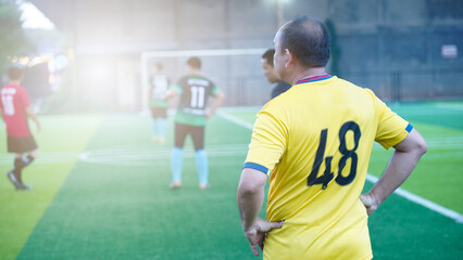 Senior male soccer player stands with his back to support yellow tiger's waist on artificial grass field.