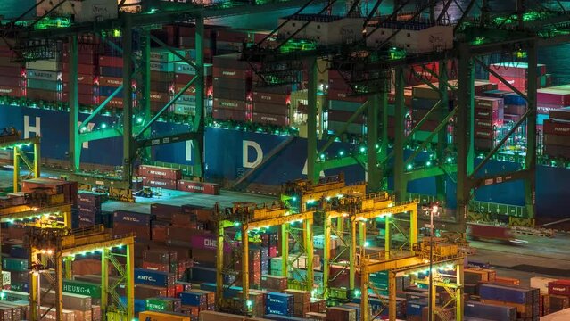Zoom out Time lapse video of working gantry cranes at Singapore container port at night.