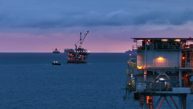 The barge, floating to the oil drilling rig, located in San Pedro Channel, USA. The illuminated offshore rig, vessels continue working in the evening time. High quality 4k footage