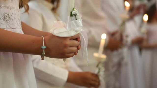 Children stand in the church at the first communion and hold lighted candles in their hands.