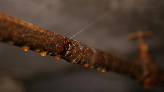 Fistula on a rusty water pipe in the basement. Pressurized water flows out of a small hole in a metal pipe. Water system leak.