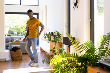 Happy african american man standing, smiling and looking away in sunny living room