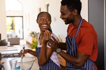 Tuinposter Happy african american couple in aprons preparing bread dough in kitchen © WavebreakMediaMicro