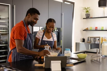 Fotobehang Happy african american couple in aprons preparing bread dough in kitchen © wavebreak3