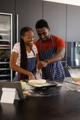 Schilderijen op glas Happy african american couple in aprons preparing bread dough in kitchen © wavebreak3