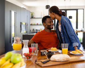 Happy african american couple embracing and serving breakfast in dining room